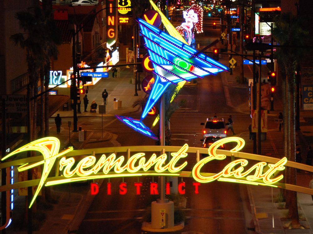 A large retro-style neon arch reading 'Fremont East District' at night, with a giant martini-glass sculpture overhead and Fremont Street stretching into the distance