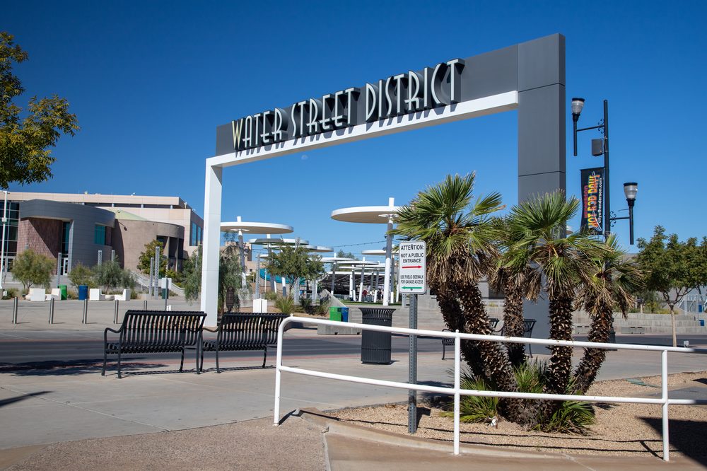 The Water Street District gateway sign in downtown Henderson, Nevada, arching over the sidewalk under a clear blue sky with palm trees below