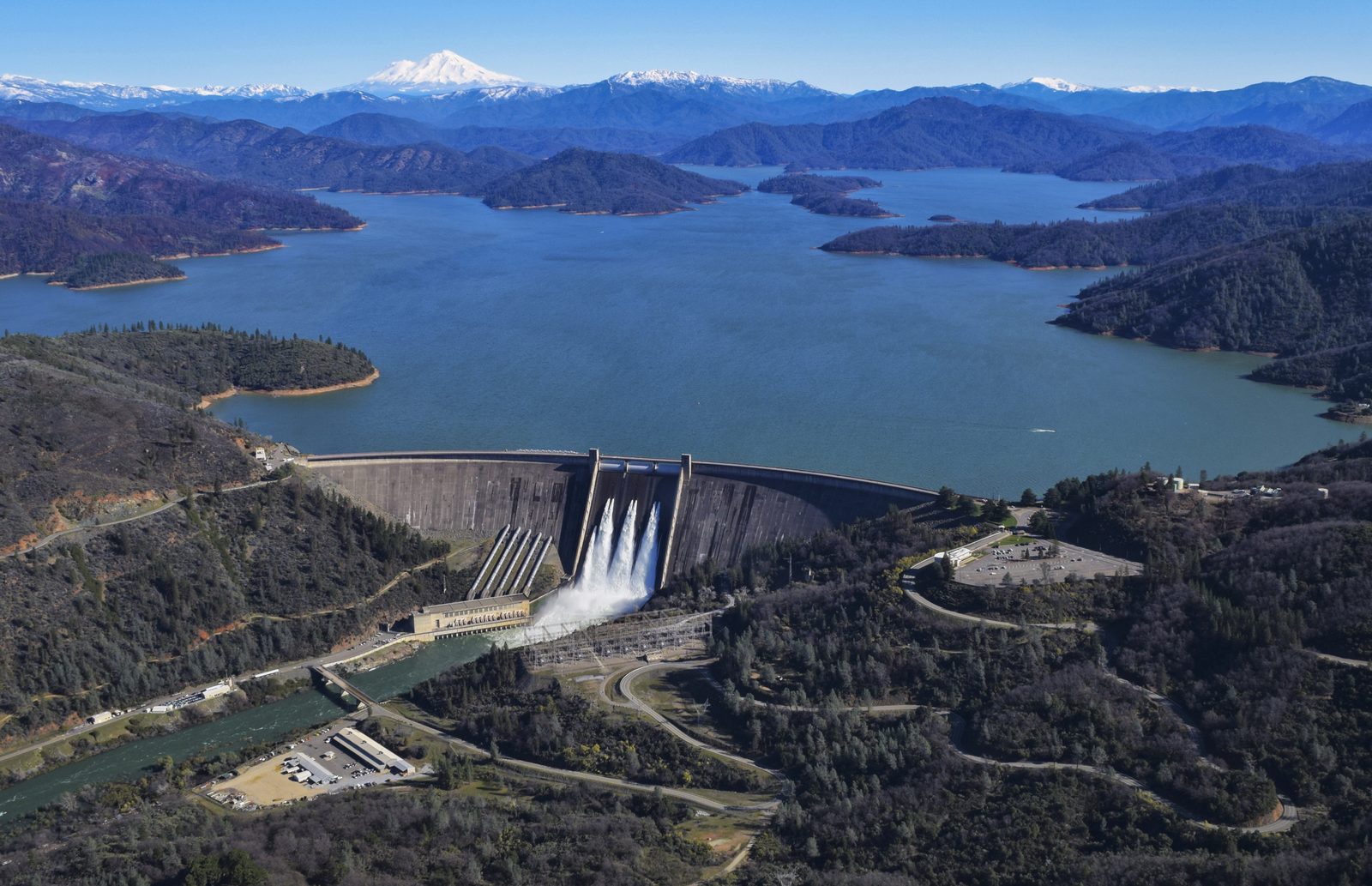 An aerial view of Shasta Dam and Shasta Lake in Northern California, showing the arch-gravity dam holding back the state's largest reservoir