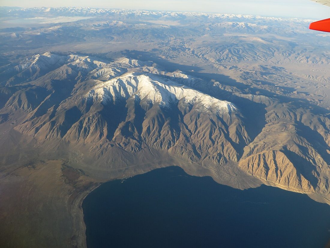 An aerial view of Walker Lake, Nevada, a blue desert lake at the base of the snow-capped Wassuk Range, seen from an airplane window