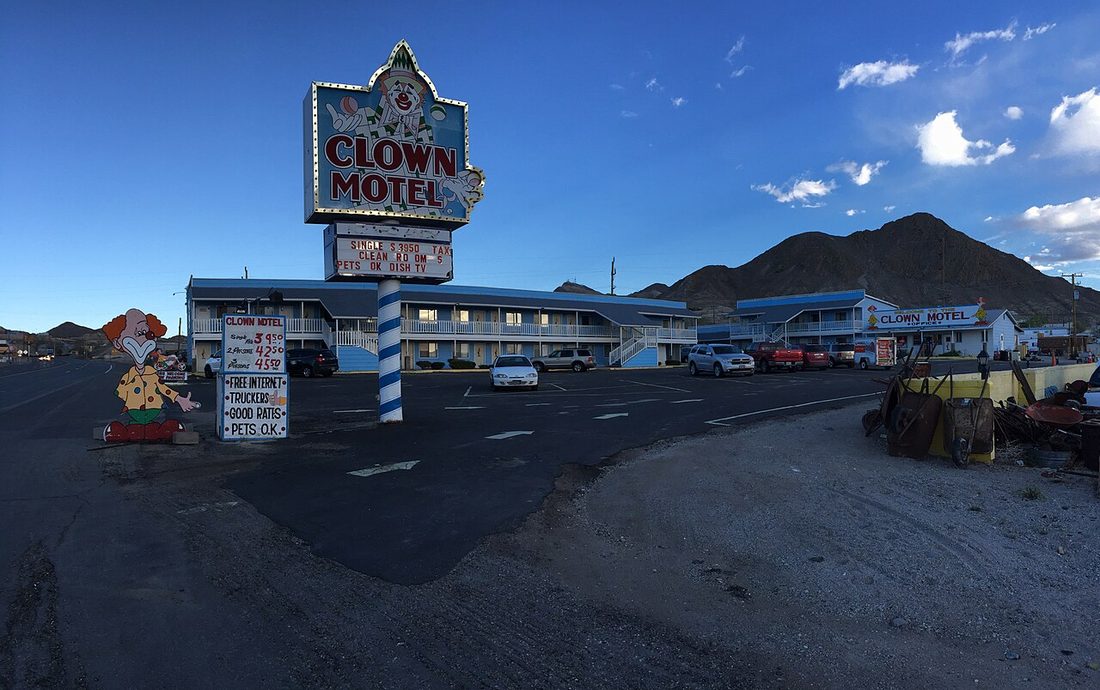 The Clown Motel sign in Tonopah, Nevada, lit up against a blue evening sky, with a large clown cutout statue and the motel building visible below