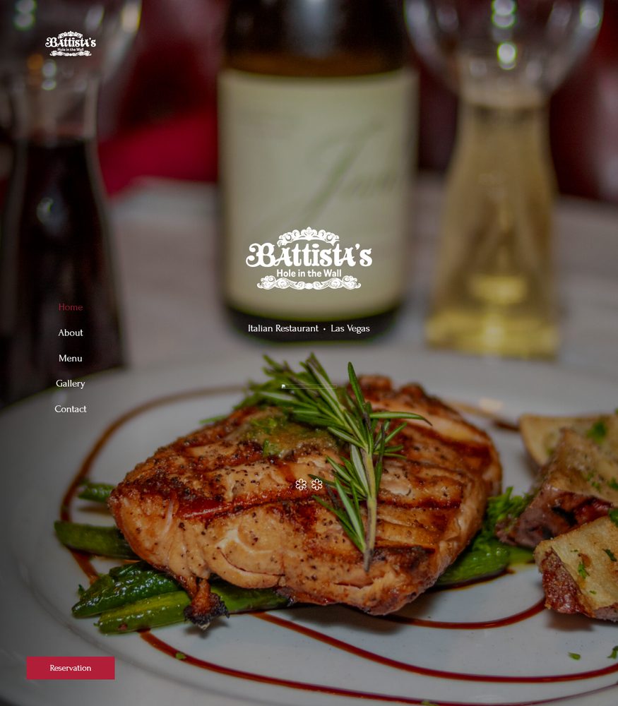 A grilled entree with asparagus at Battista's Hole in the Wall in Las Vegas, with a bottle of house wine and the restaurant's logo in the background
