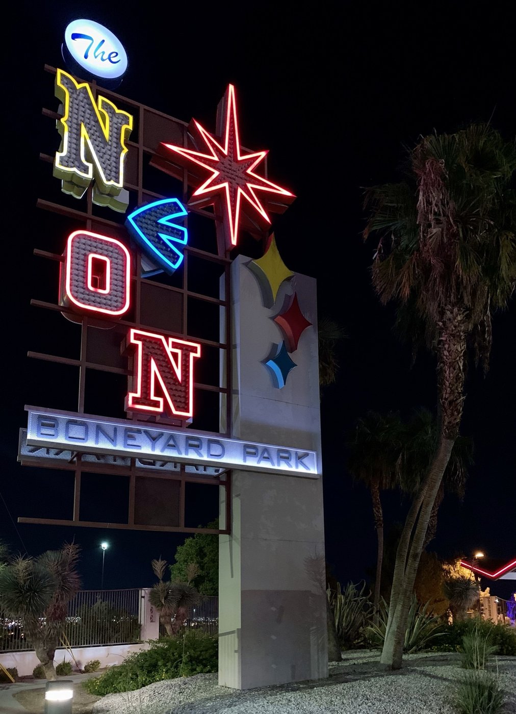 The Neon Museum's Boneyard Park entrance sign at night, spelling out NEON in letters individually styled after the Golden Nugget, Caesars Palace, Binion's Horseshoe, and Desert Inn signs, above a lit BONEYARD PARK marquee