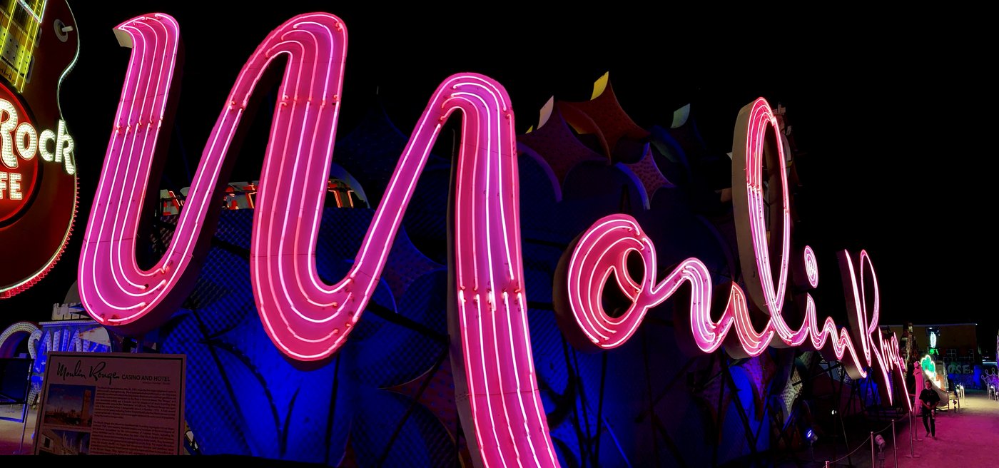 The restored Moulin Rouge neon sign in pink cursive script at the Neon Museum, with an information panel telling the hotel's history mounted beside it