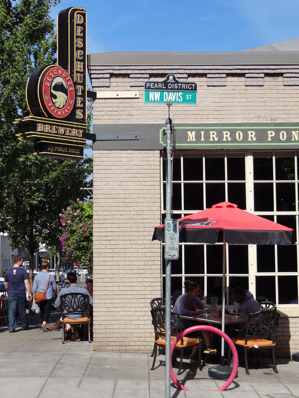 The Deschutes Brewery neon sign outside its Portland Public House on the corner of NW 11th Avenue and NW Davis Street in the Pearl District, with outdoor cafe seating and a red umbrella
