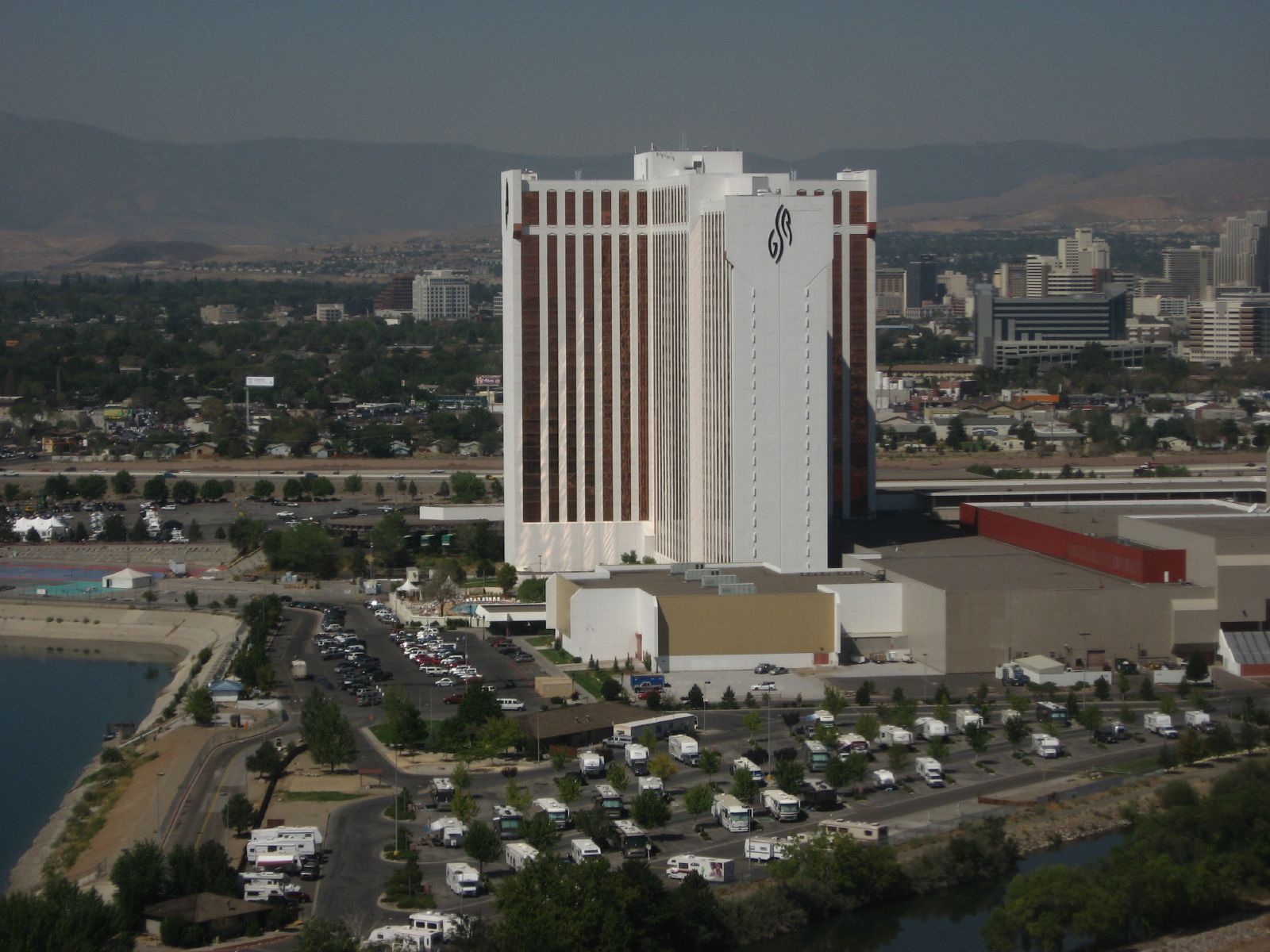 An aerial view of the Grand Sierra Resort's tall white and brown hotel tower on the eastern edge of Reno, Nevada, with the downtown Reno skyline visible in the background and mountains beyond