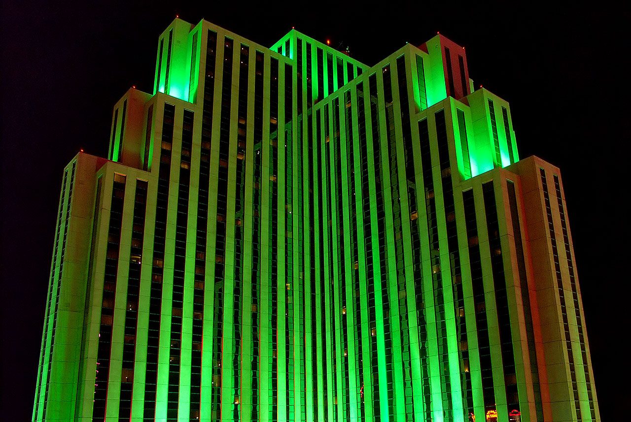 The upper floors of the Silver Legacy Resort Casino tower in Reno at night, lit entirely in bright emerald green against a black sky