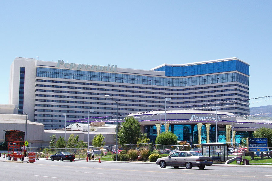 The exterior of the Peppermill Reno hotel and casino, a tall tan hotel tower with a curved teal-glass entrance canopy and the Peppermill name in large letters on the building's facade