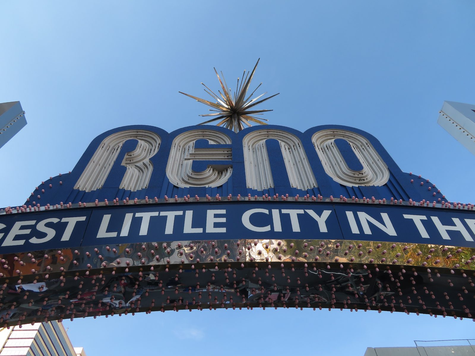The Reno Arch spanning Virginia Street at night, its blue and silver neon lettering reading 'RENO' above a sign reading 'The Biggest Little City in the World'