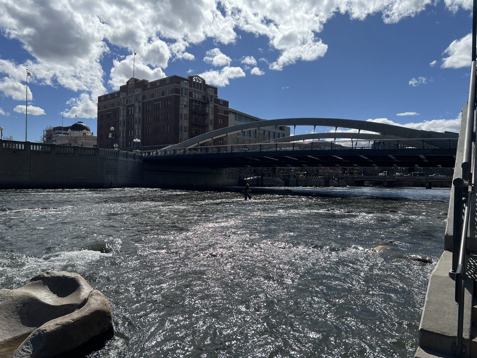 The Truckee River Whitewater Park in downtown Reno, Nevada, showing rapids flowing under a pedestrian bridge with the historic Riverside Hotel building and a modern arched footbridge in the background
