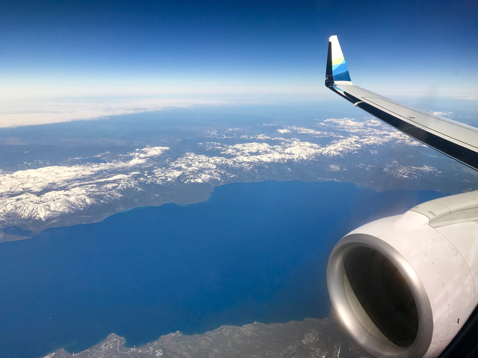 An aerial view of Lake Tahoe's deep blue water surrounded by forested mountains, taken from a small plane