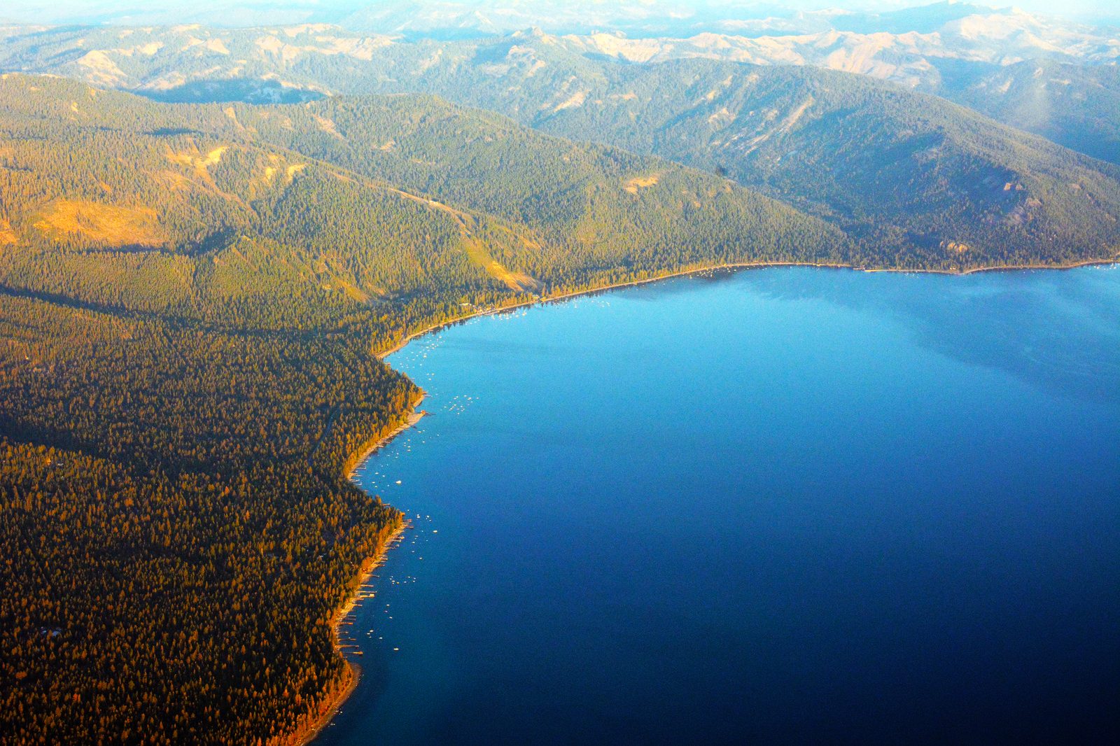 An aerial view of North Lake Tahoe, showing the deep blue water meeting a shoreline of pine forest and mountains