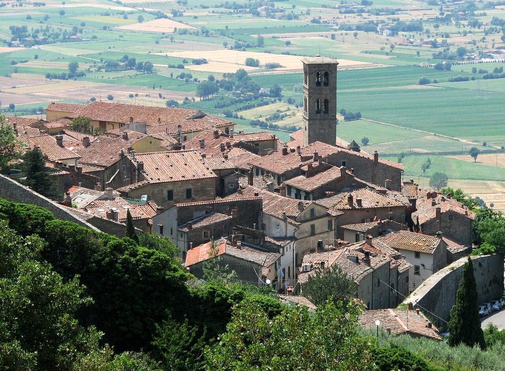 Wikipedia's Cortona article showing an aerial photo of the walled hilltop town overlooking the Val di Chiana, with the town's coat of arms in the infobox below