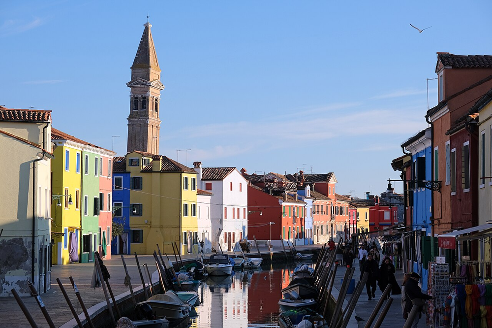 Wikipedia's Burano article showing a photo of the island's brightly colored houses along the Rio Giudecca canal, with the leaning campanile of San Martino church in the background